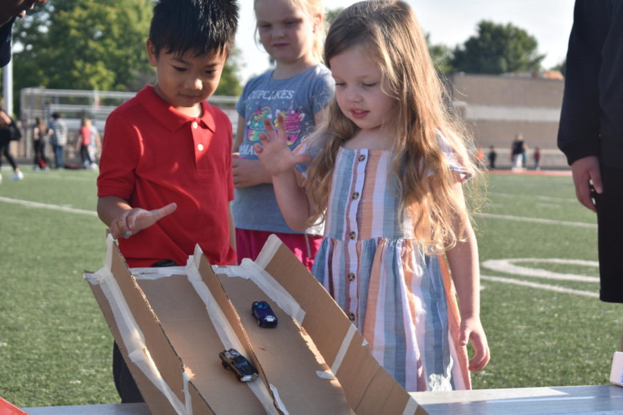 Children participate in an experiment using toy racecars and momentum. 