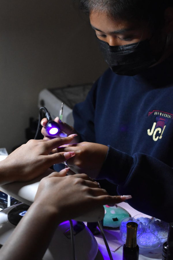 Senior Tha Zi holds up a UV light to a customers nails at her place of business on Friday, Oct. 7. This set took an hour. 
