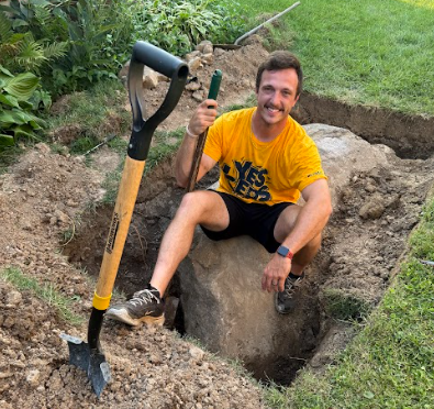 Dudas sits in the hole he dug in his yard with the boulder he excavated. (photo contributed by Brendan Dudas)